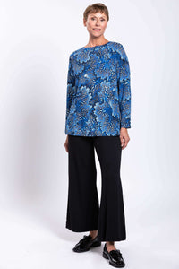 Woman in blue botanical print top standing in black pants