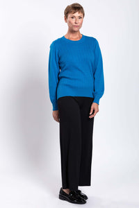 Woman in blue crew neck cable knit sweater with hands by her side