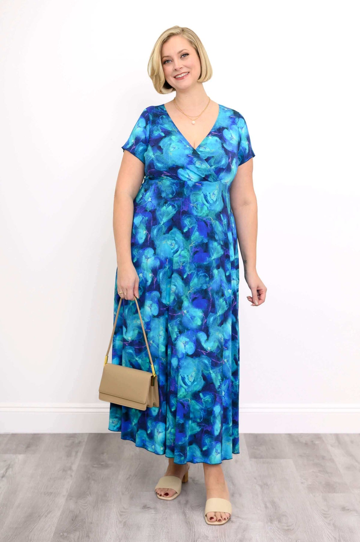 Woman wearing a blue floral bamboo maxi dress, holding a beige handbag and smiling