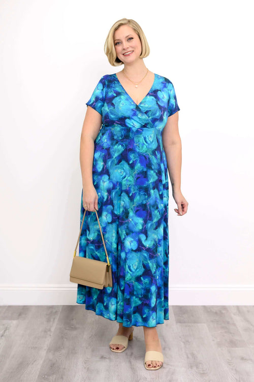 Woman wearing a blue floral bamboo maxi dress, holding a beige handbag and smiling