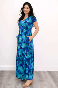 Woman in a blue and teal floral bamboo maxi dress with hands in pockets, smiling