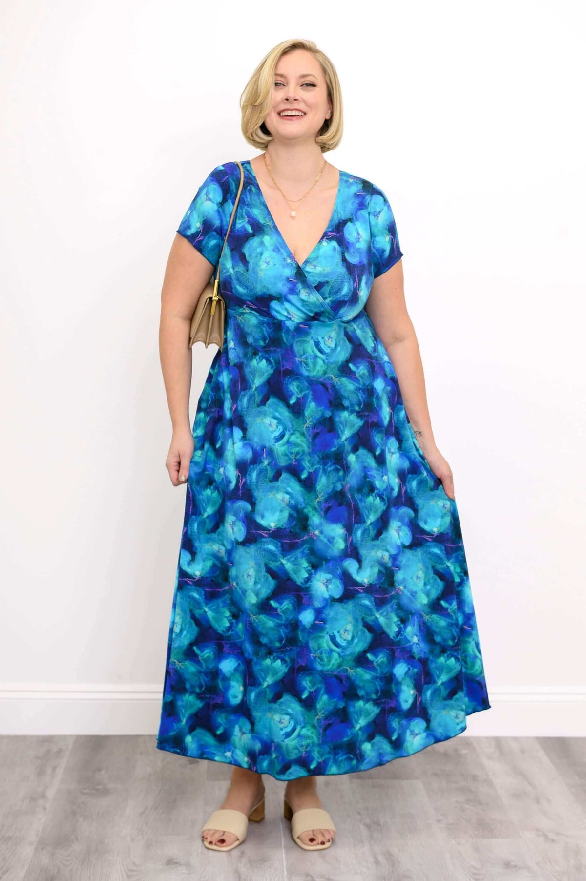 Woman smiling in a blue floral bamboo dress, hands resting on skirt pockets