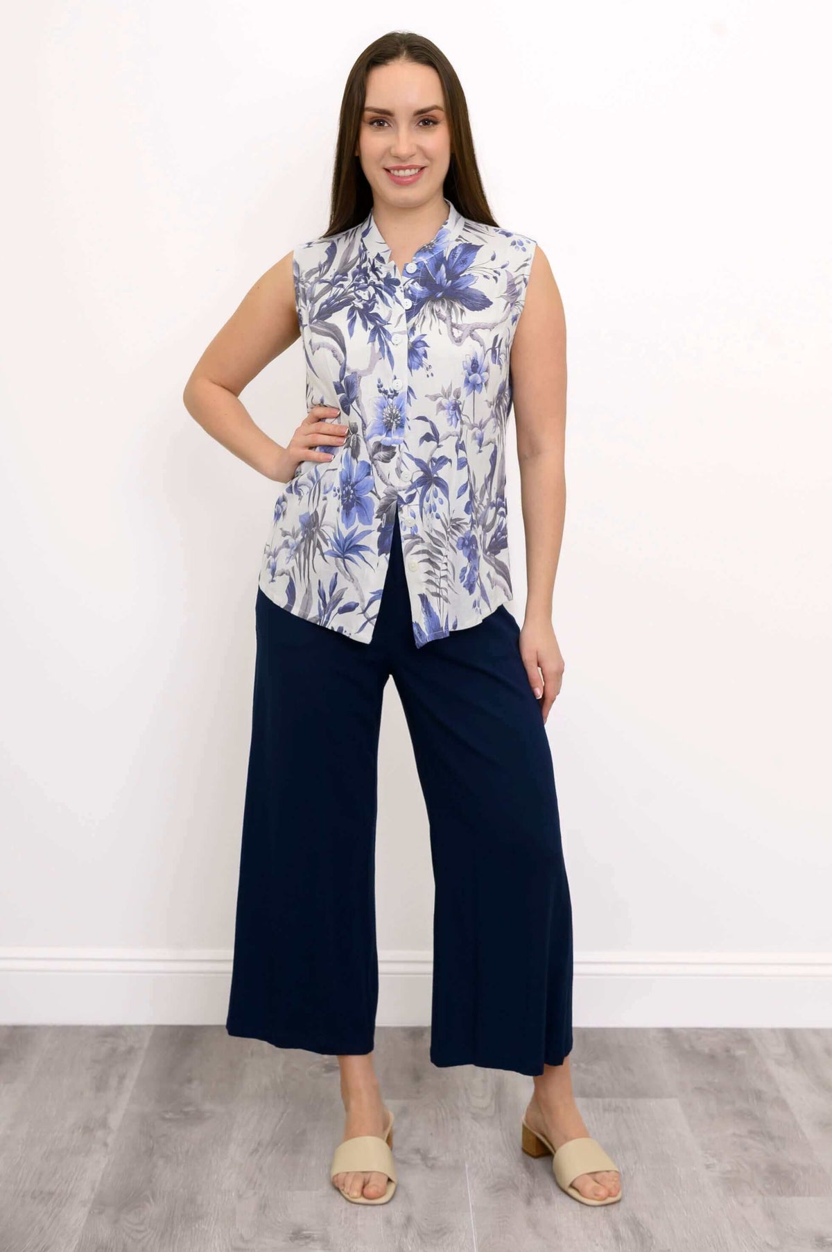 Woman standing facing forward in blue floral sleeveless blouse and navy pants