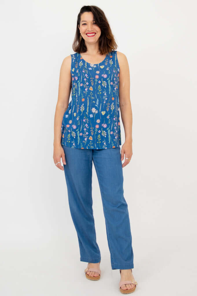 Woman wearing blue floral tank and blue pants, smiling, arms relaxed at sides