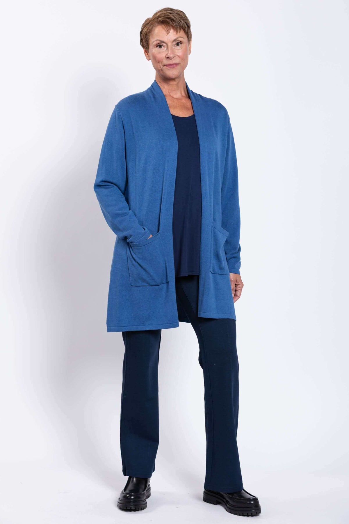 Woman in a blue open-front cardigan and navy pants standing at a slight angle