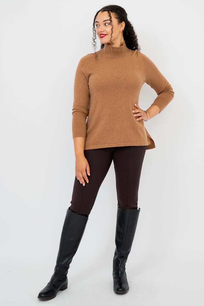 Woman in camel sweater with hand on hip, showing side hi-lo hem