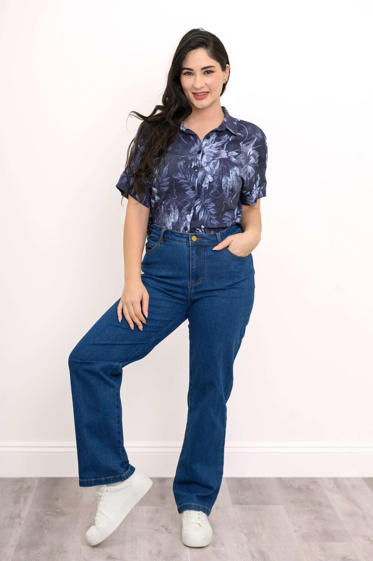 Woman in floral blouse and blue jeans, smiling with one leg raised