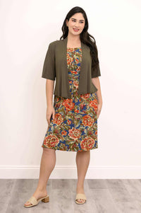 Woman in floral dress and olive short-sleeved jacket standing on wood floor