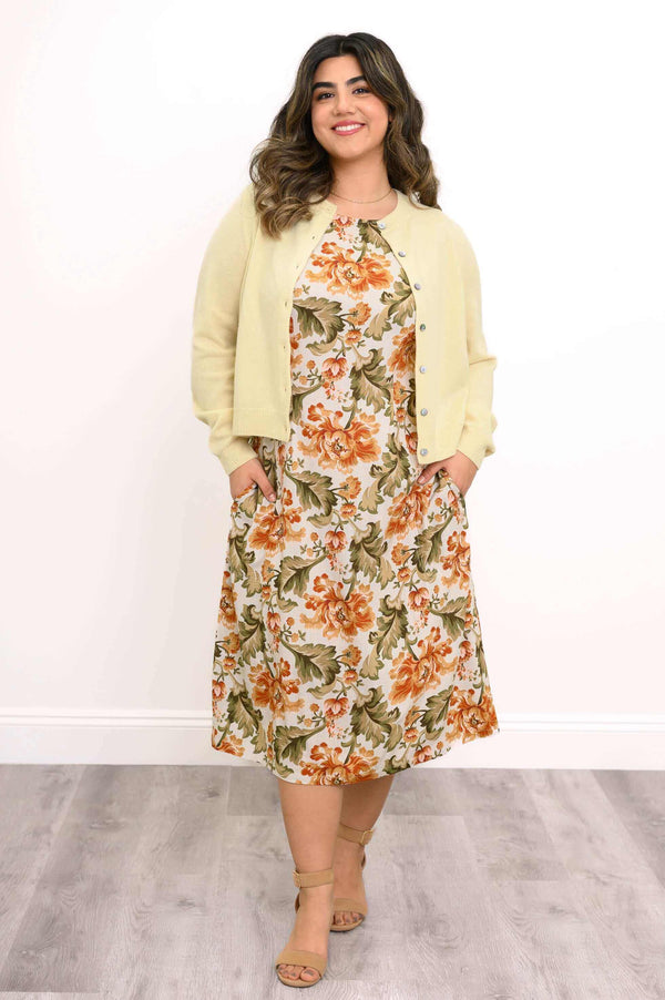 Woman in floral dress with cardigan, hands in pockets, smiling