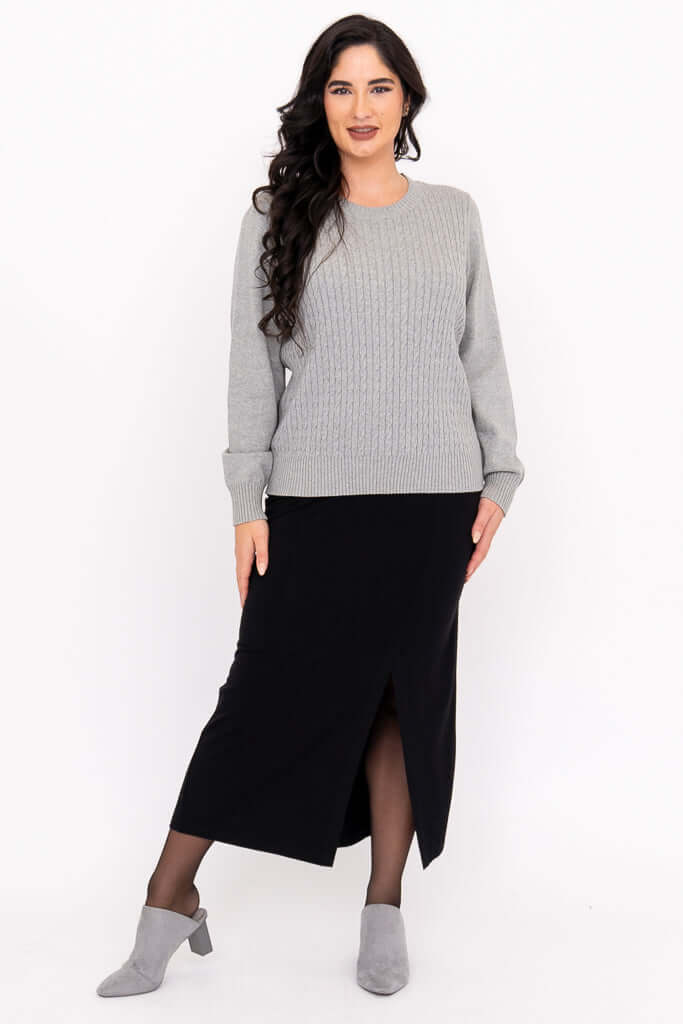 Woman in grey cable knit sweater and black midi skirt