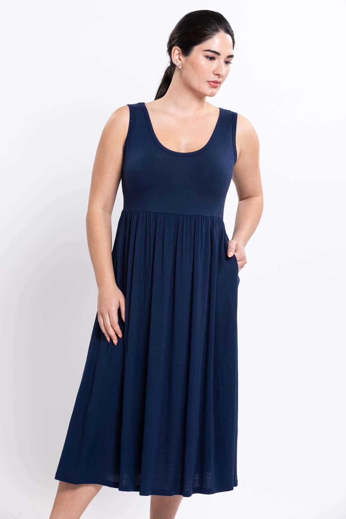 Woman in indigo sleeveless midi dress with hand in pocket, looking aside