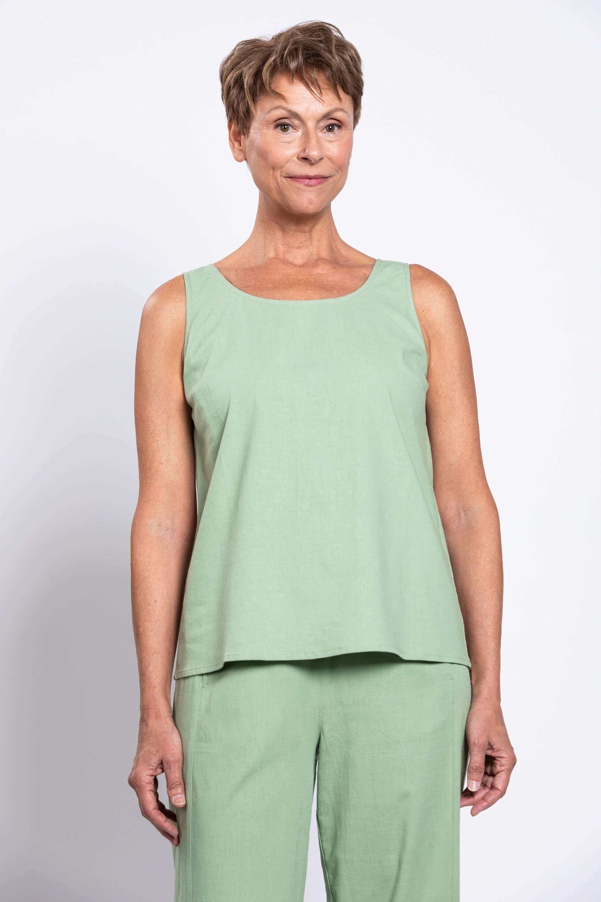 Woman wearing a sleeveless light sage green tank top, front view, cropped at waist