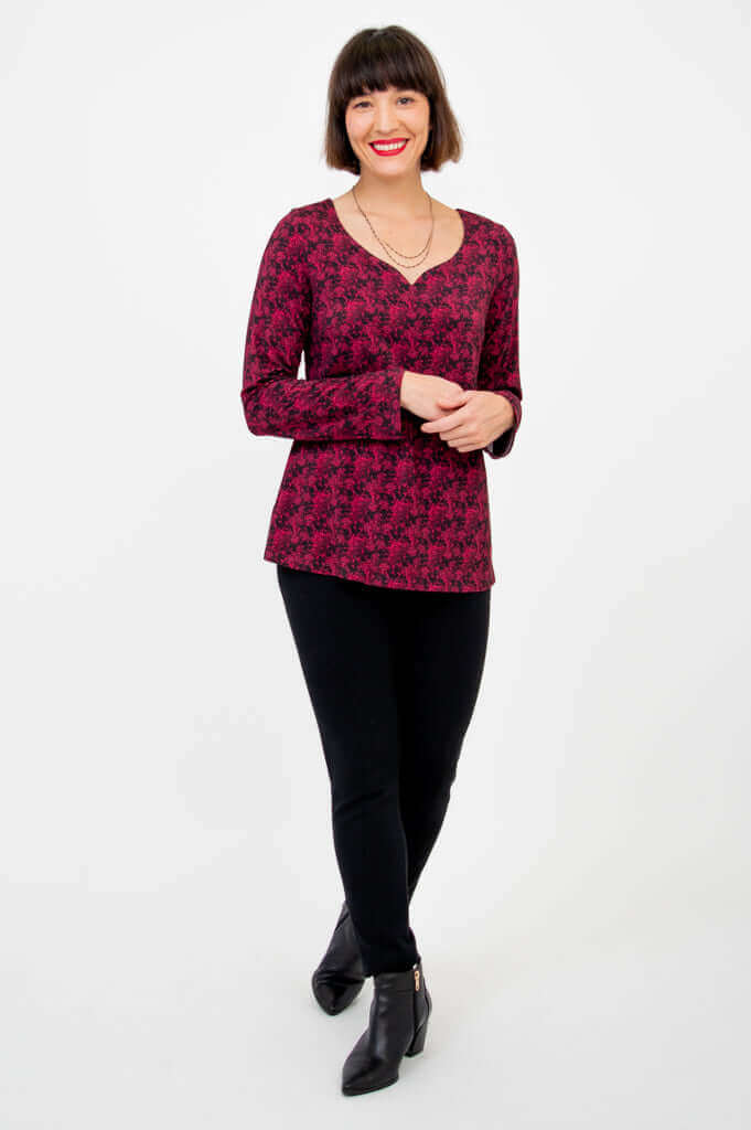 Woman smiling in magenta sweetheart neckline top with arms folded, wearing black pants