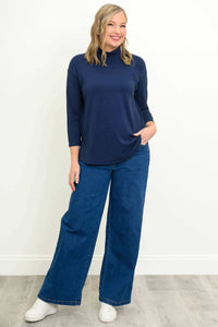 Woman in navy mock neck top and wide-leg jeans with a relaxed pose