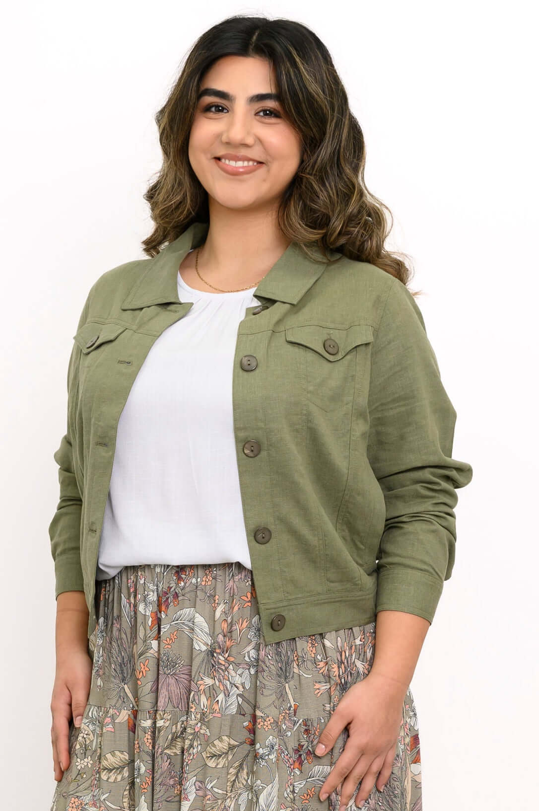 Woman wearing an olive green jean-style jacket with a white top and floral skirt
