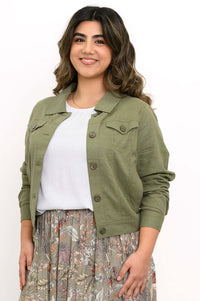 Woman wearing an olive green jean-style jacket with a white top and floral skirt