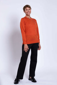 Woman in orange V-neck merino wool sweater, standing at a slight angle, smiling