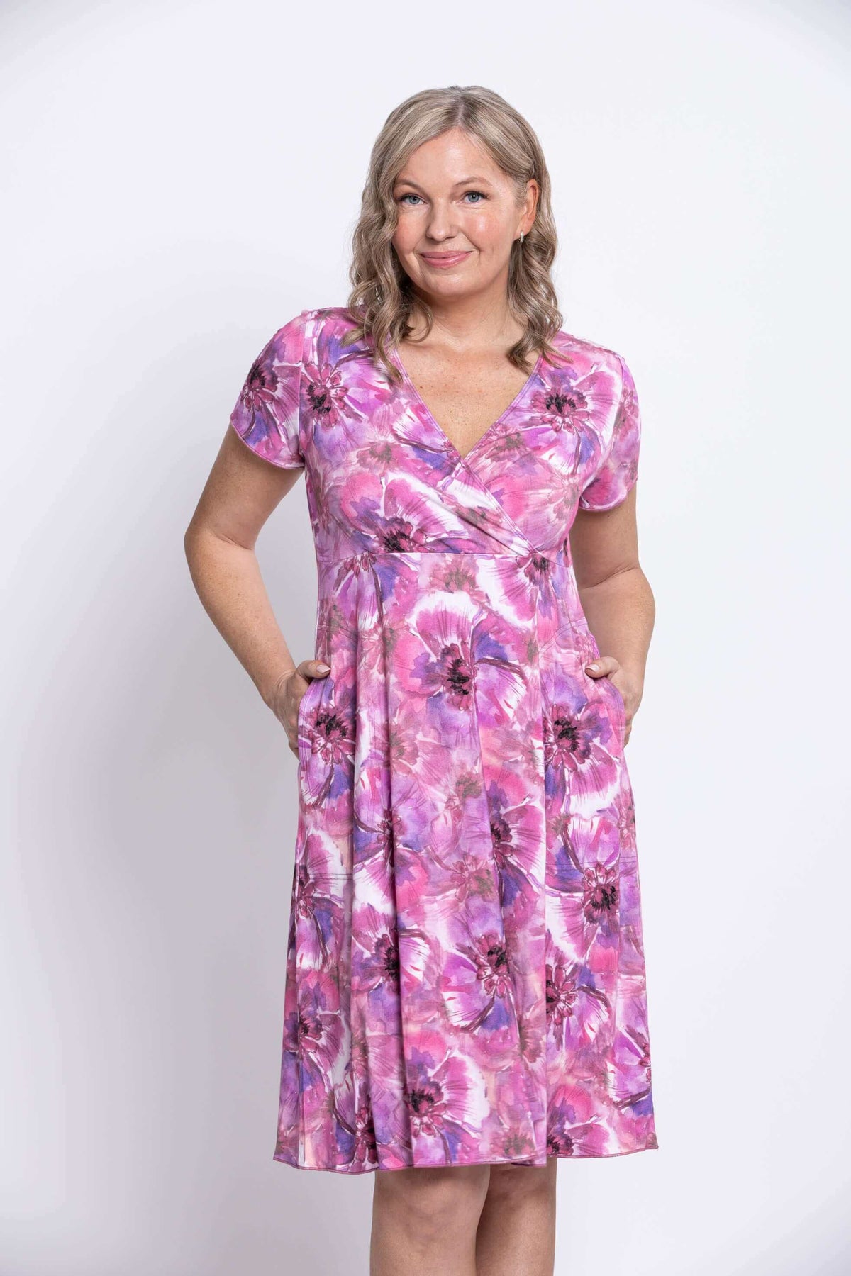 Woman smiling in V-neck pink and purple floral cross-front dress with pockets