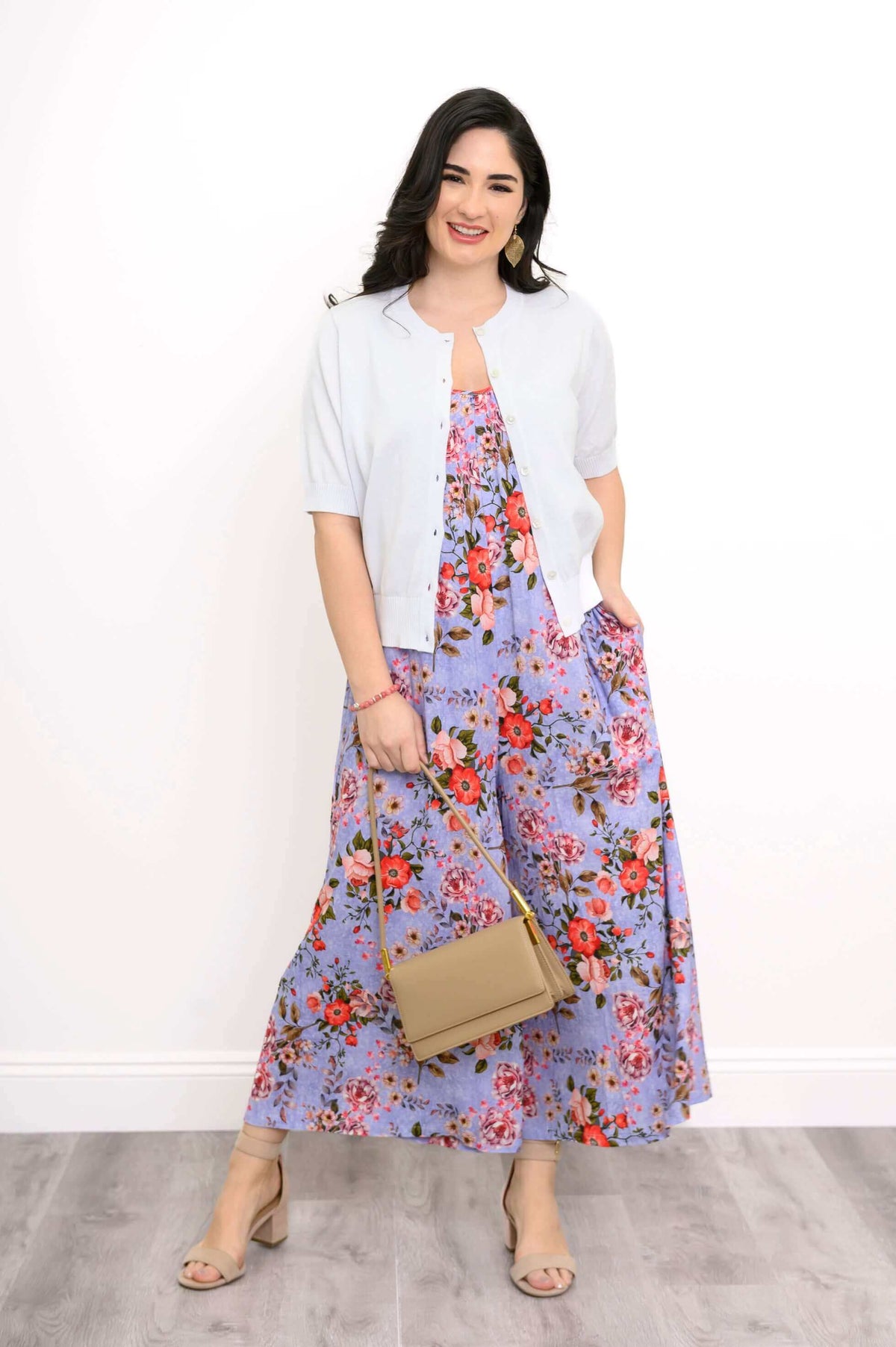 Woman styled in a purple floral jumpsuit with a light cardigan and tan handbag