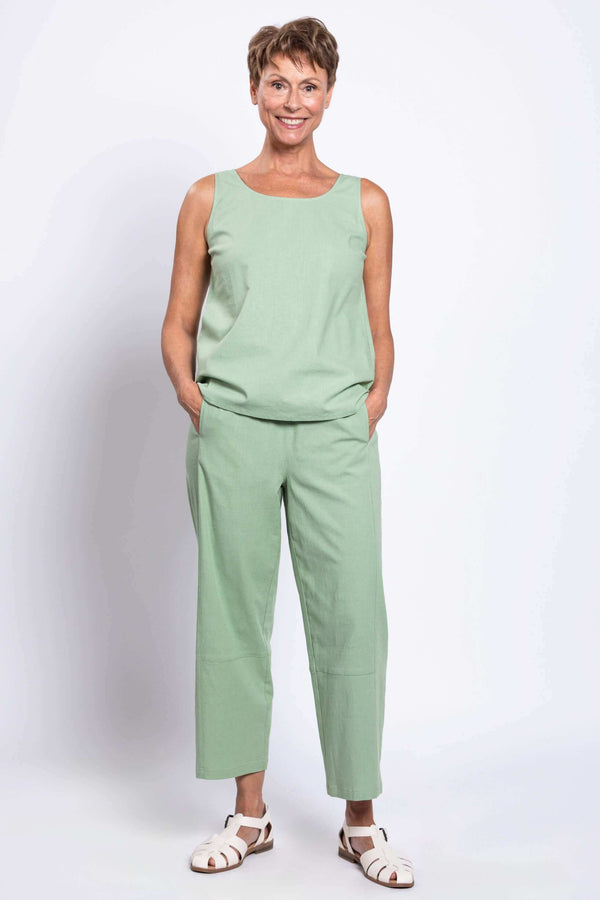 Woman wearing sage green cropped barrel-leg linen pants and matching sleeveless top, hands in pockets