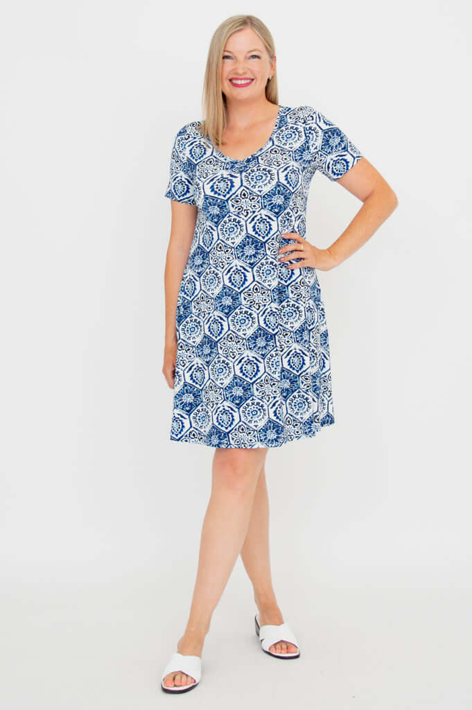 Woman wearing a short sleeve blue and white mosaic print dress, smiling and posing with hand on hip