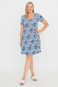 Woman wearing a short sleeve blue and white mosaic print dress, smiling and posing with hand on hip