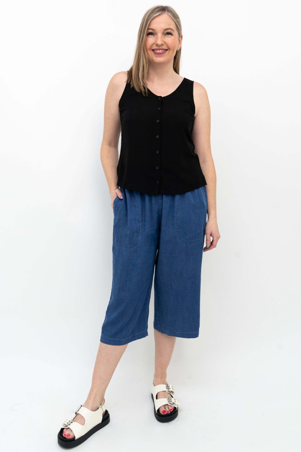 Woman in sleeveless black top wearing blue flowy tencel denim capris
