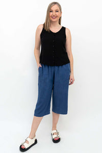 Woman in sleeveless black top wearing blue flowy tencel denim capris