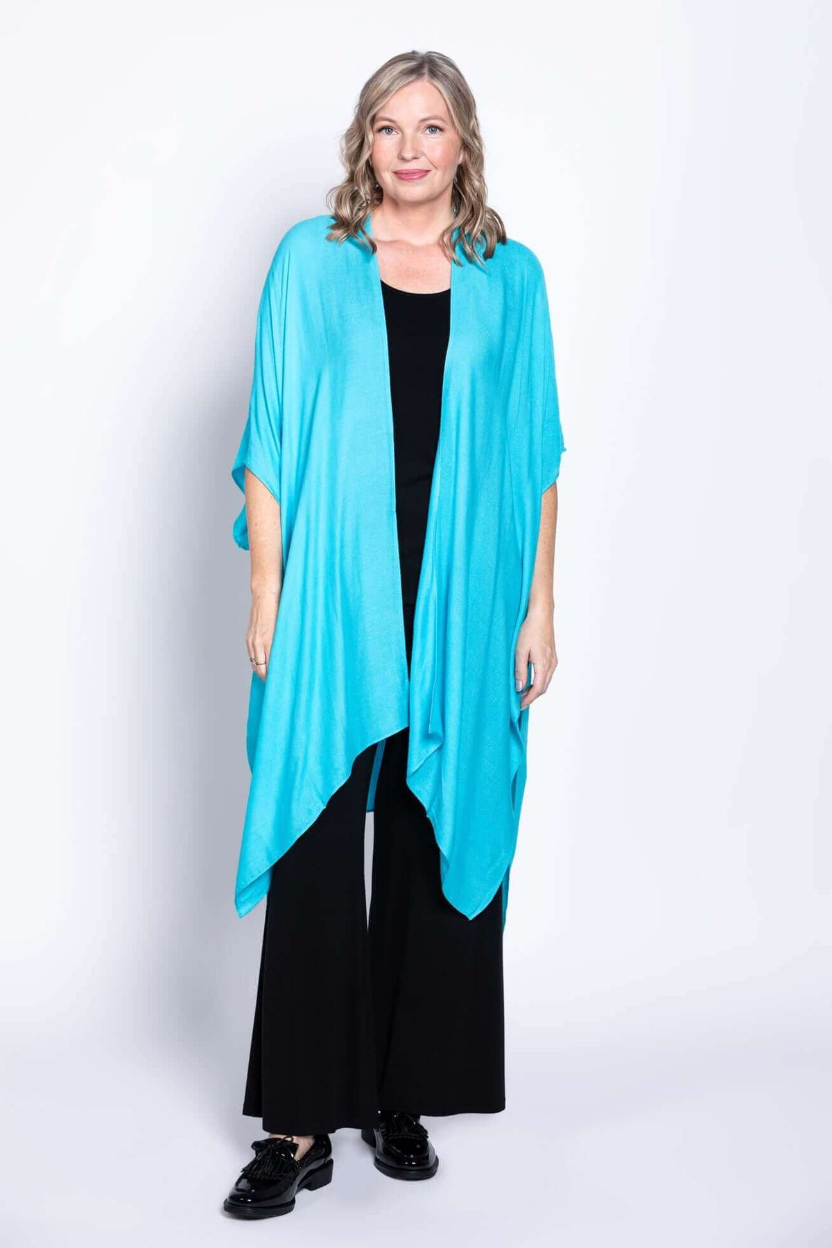Woman wearing a turquoise kimono wrap over black outfit, standing and smiling