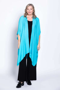 Woman wearing a turquoise kimono wrap over black outfit, standing and smiling
