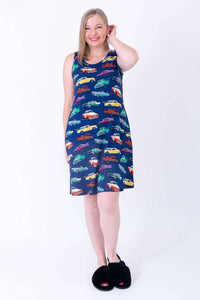 Woman in blue sleeveless dress with vibrant car print, smiling with hand on head
