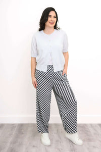 Woman in white short-sleeve cardigan and checkered pants, standing and smiling