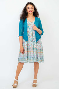 Woman layering a teal cardigan over a floral tiered dress with scoop neckline