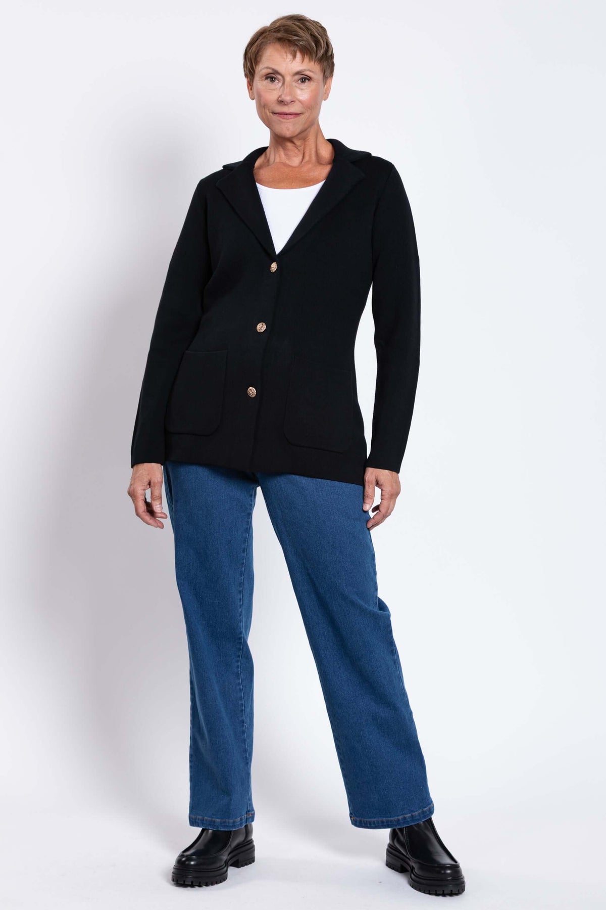 Woman standing in the Margaret Jacket, black knit with gold buttons and front pockets