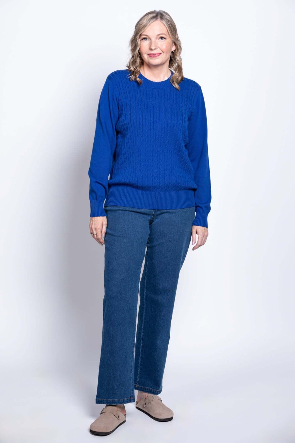 Woman modeling blue cable knit sweater, straight jeans, and beige clogs, front angle