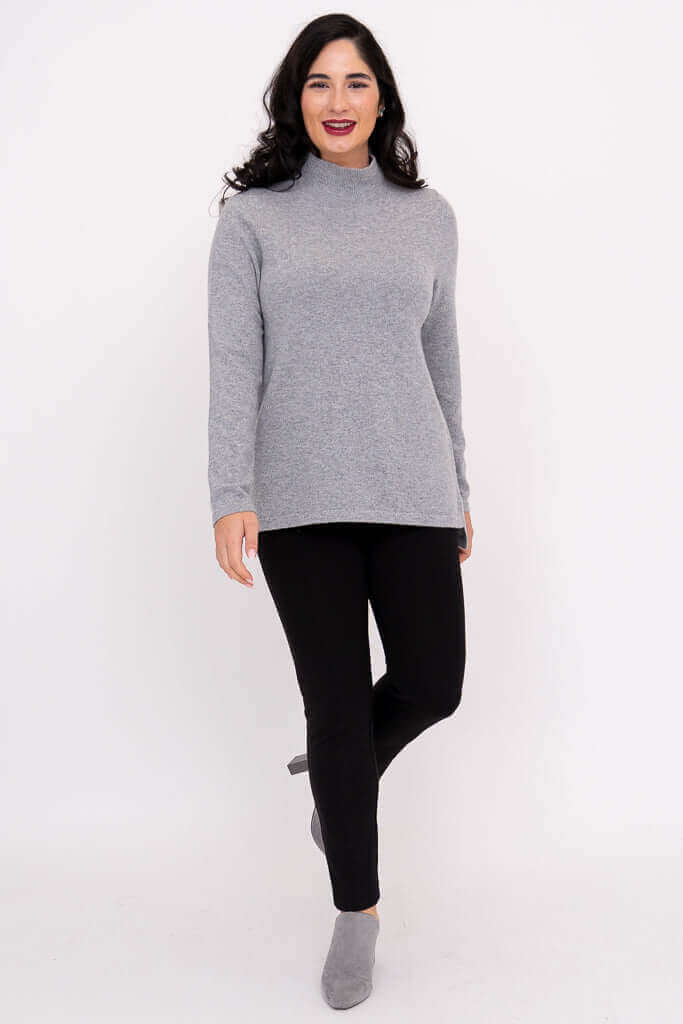Woman standing in a grey mock neck sweater and black pants with grey shoes