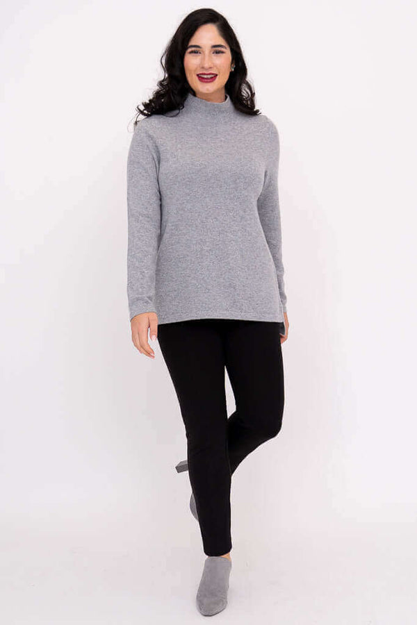Woman standing in a grey mock neck sweater and black pants with grey shoes