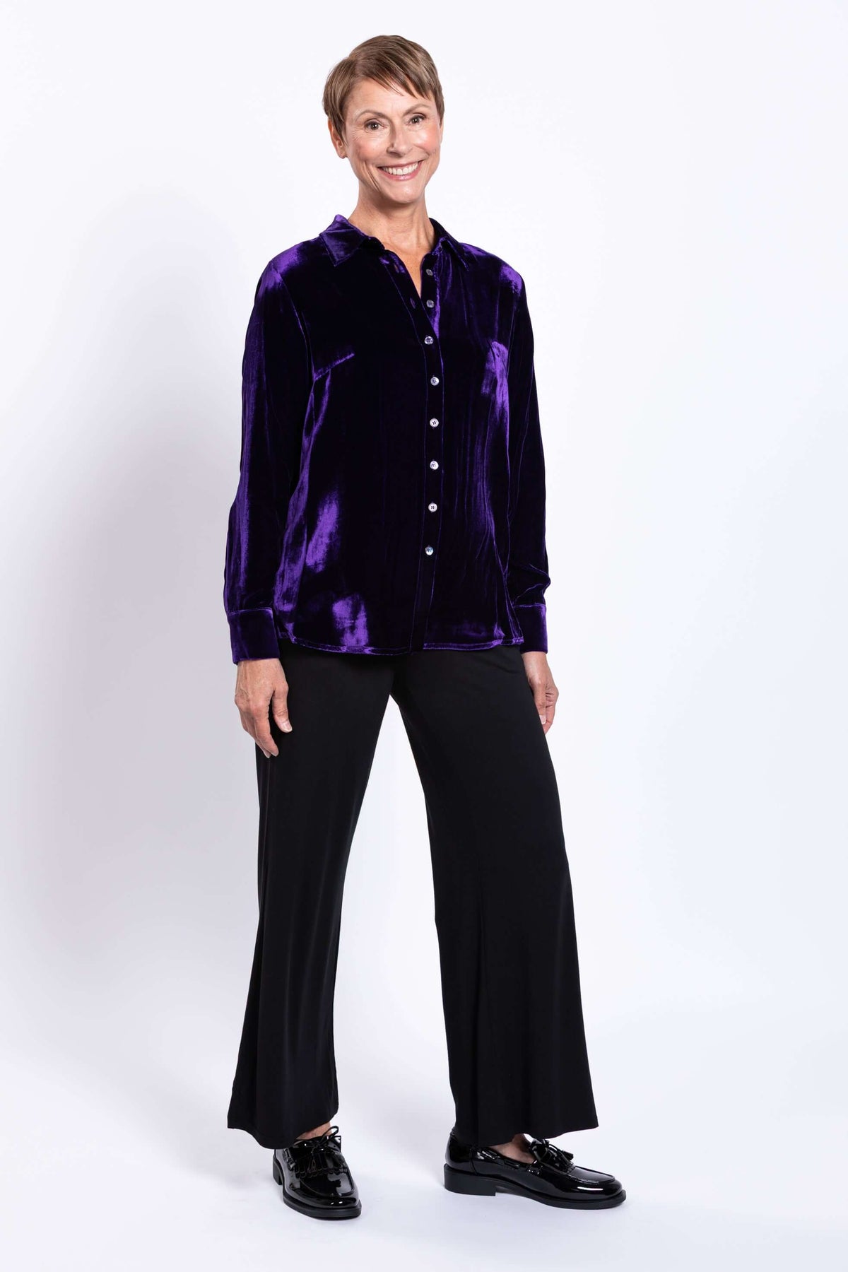 Woman smiling and modeling purple silk velvet blouse in a relaxed stance