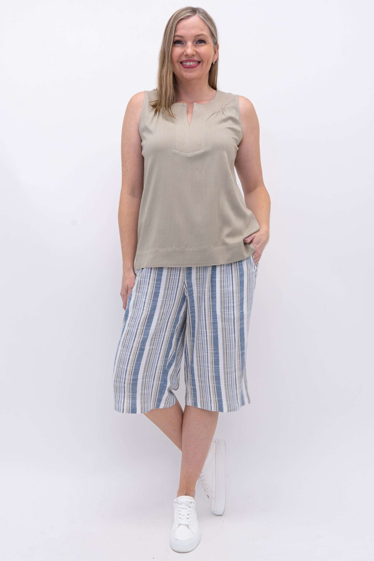 Woman wearing blue and white striped Bermuda shorts with beige sleeveless top