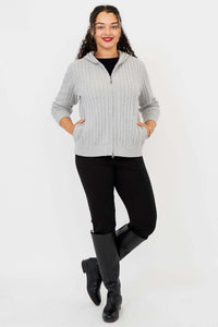 Woman posing in light grey cable knit hoodie with both hands in pockets