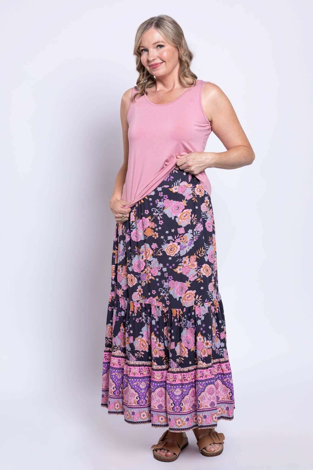 Woman posing in Tibby floral skirt and pink tank top, hand at waistband