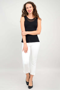Woman posing in black mesh tank and white pants, arms crossed