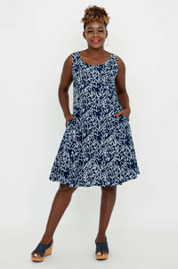 Woman posing in a navy and white sleeveless dress with hands in pockets