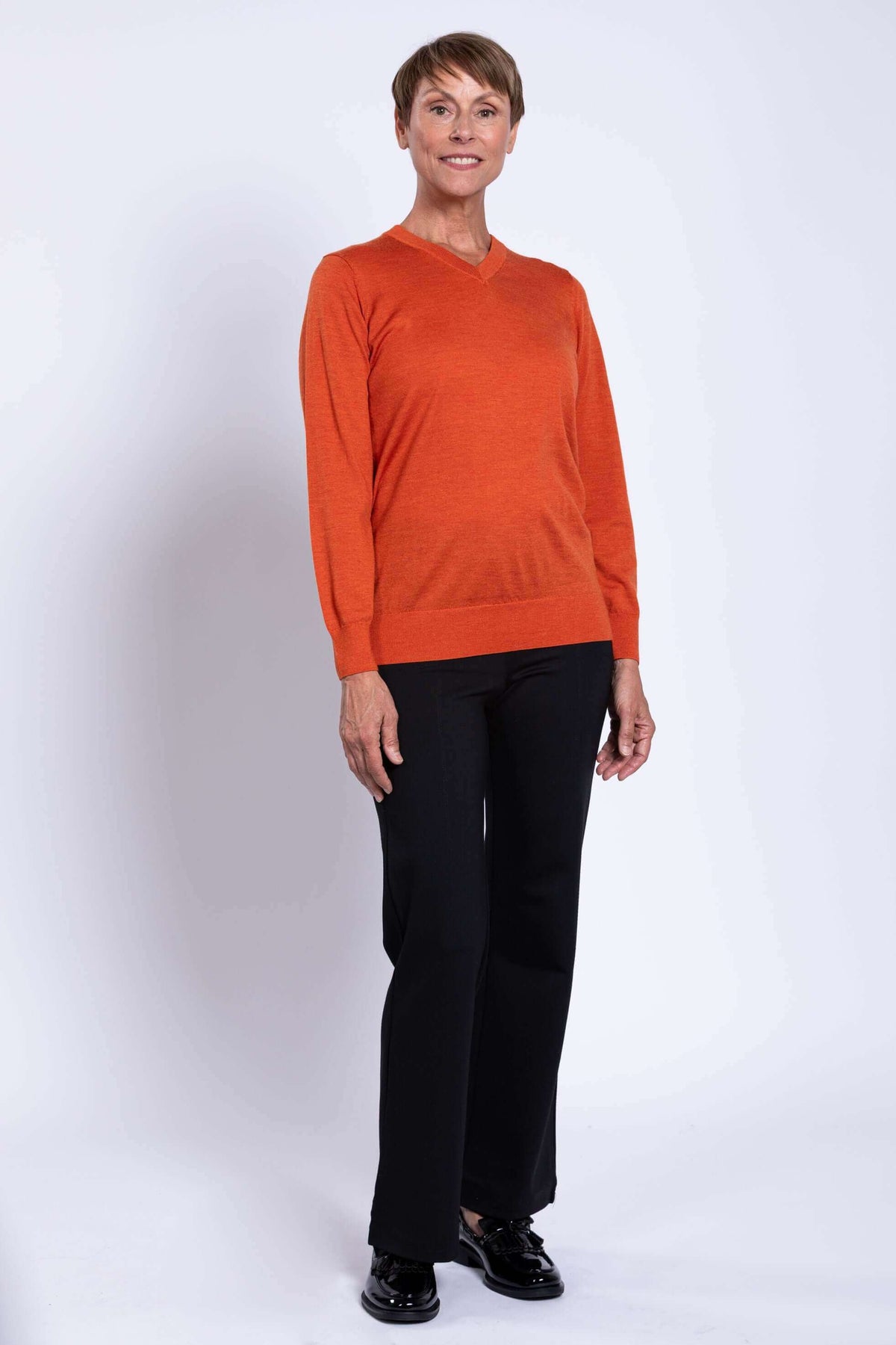 Woman posing in orange merino wool V-neck sweater and black pants, angled view