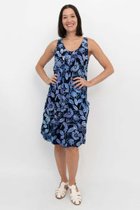 Woman smiling in a sleeveless navy blue floral dress with hands on hips, front view