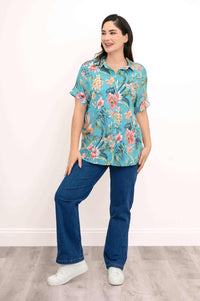 Woman posing in turquoise floral blouse with jeans and white sneakers