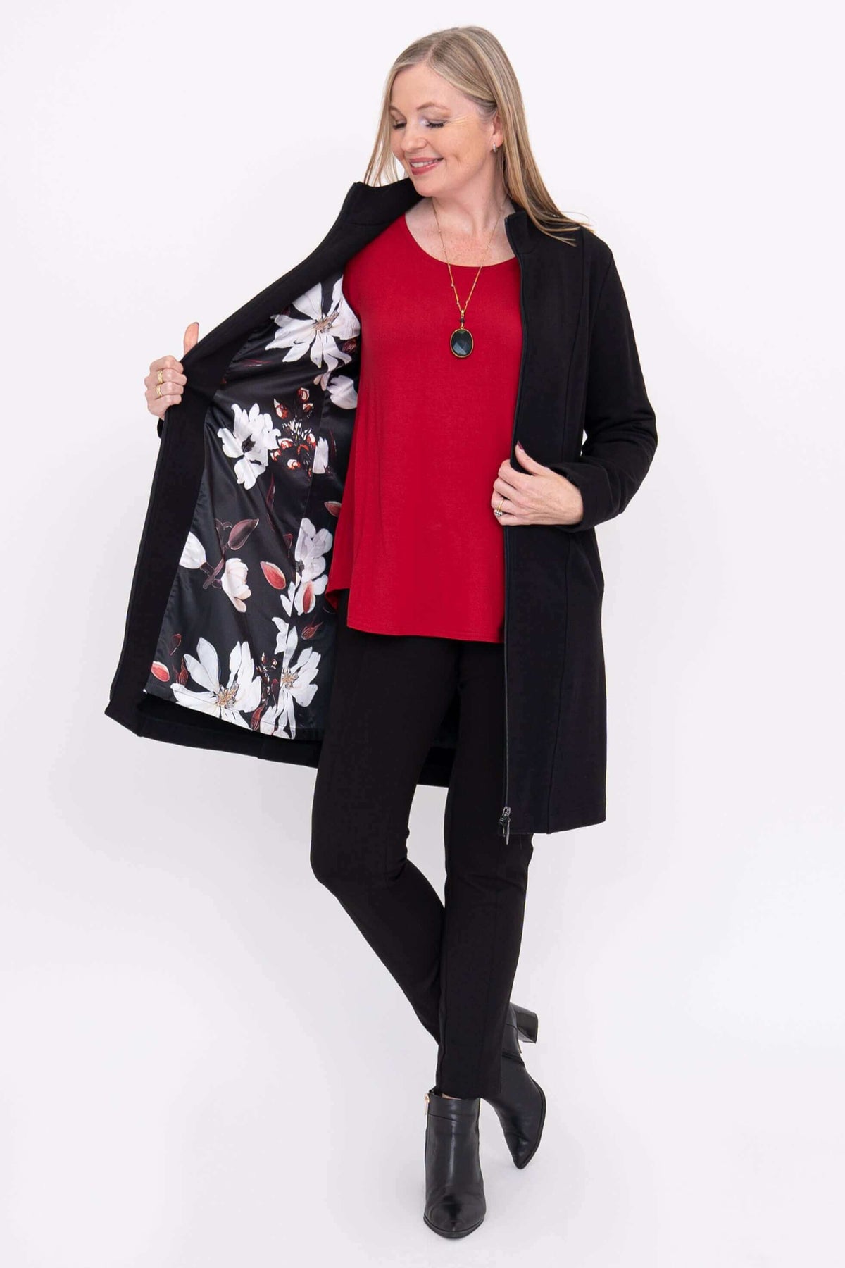 Woman showing floral lining of black coat, wearing red top and black pants