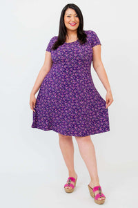 Woman in a flowing violet floral dress, holding out the skirt to show A-line shape