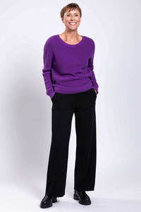 Woman smiling in a purple knit sweater and black wide-leg pants, full body view