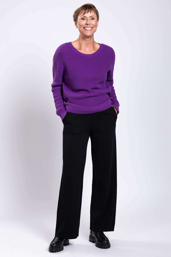 Woman smiling in a purple knit sweater and black wide-leg pants, full body view